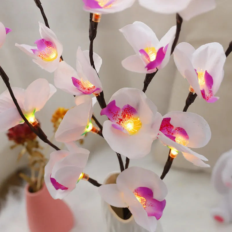Pink fabric and plastic LED Phalaenopsis orchid branch light, 65cm long, on a table providing warm white ambient glow.