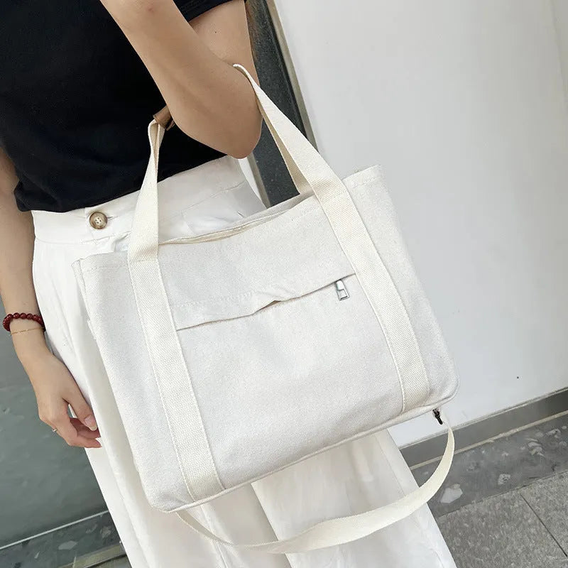 A horizontal square canvas tote bag in army green with a cross-body strap and visible sewing lines.