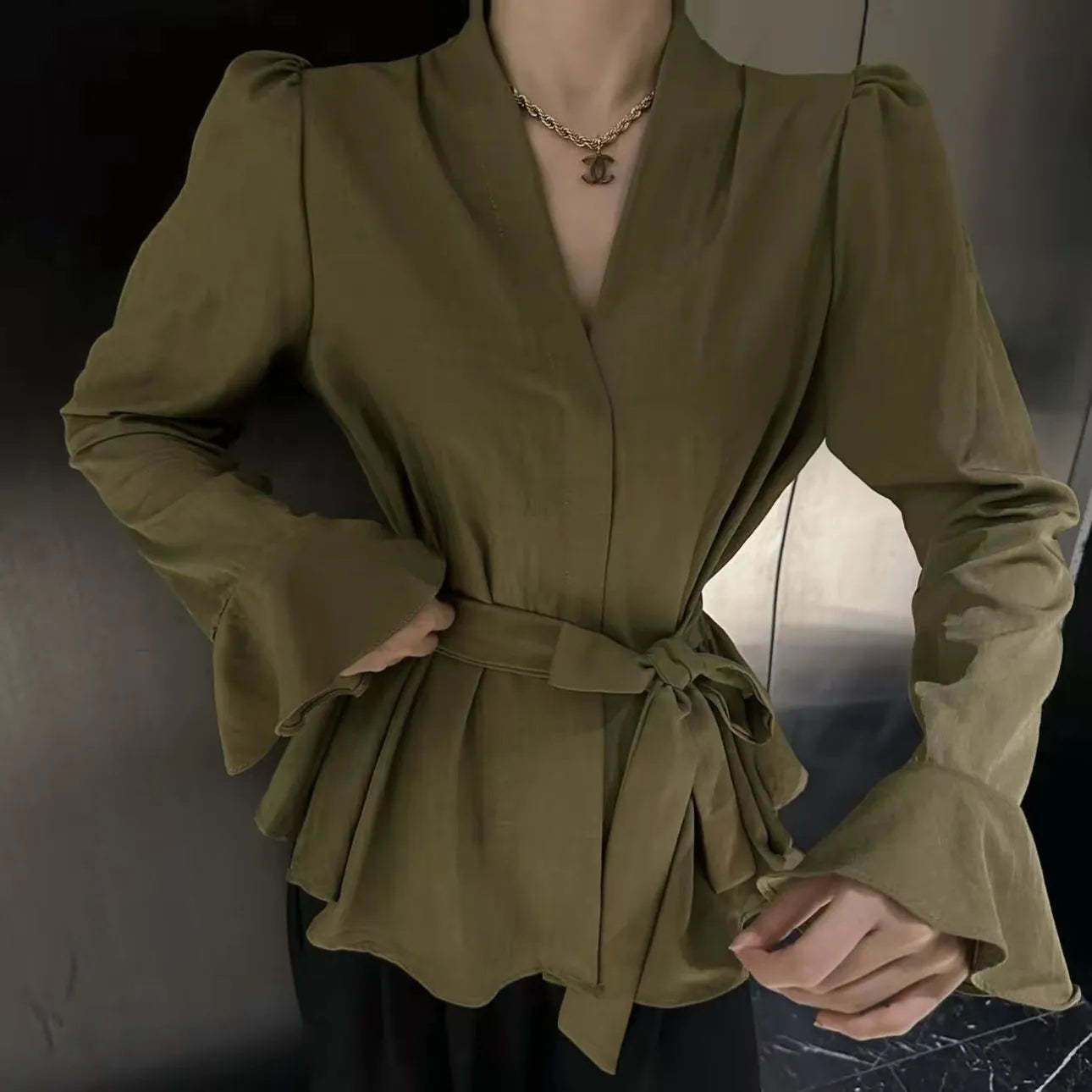 A woman wearing a black French-style shirt with an irregular collar and long bell sleeves.