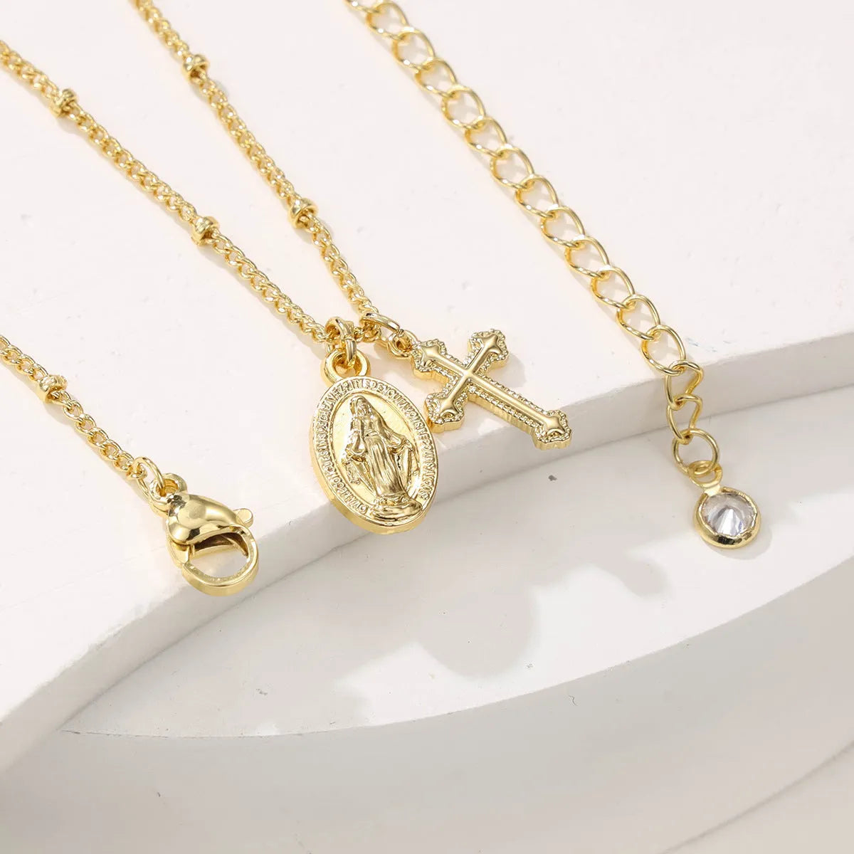 Geometric gold Virgin Mary and cross pendant necklace on a chain, showing minimalist design.