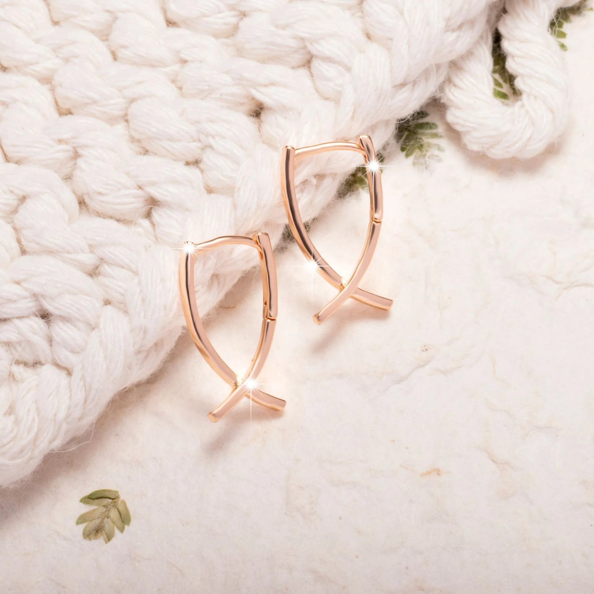 A pair of rose gold coloured cross shaped earrings on a copper base.