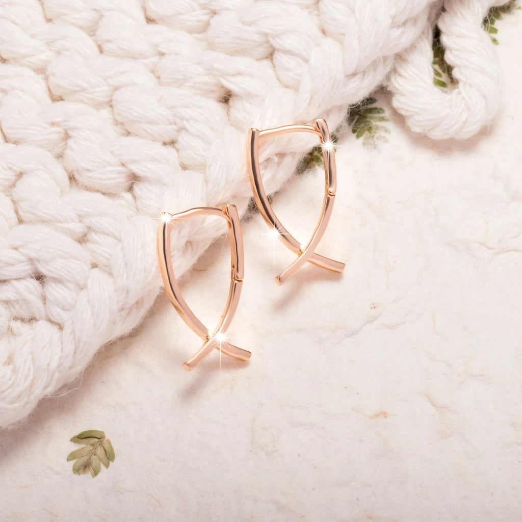 Rose gold coloured copper cross shaped earrings on a flat surface.
