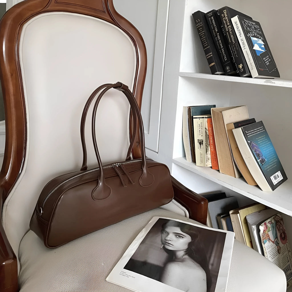 Women's solid colour genuine cowhide leather oval single-shoulder bag in brown with visible sewing thread detail.
