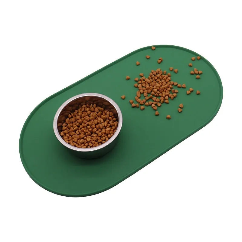Green silicone cat feeding mat with raised edge under a ceramic bowl on a wooden floor