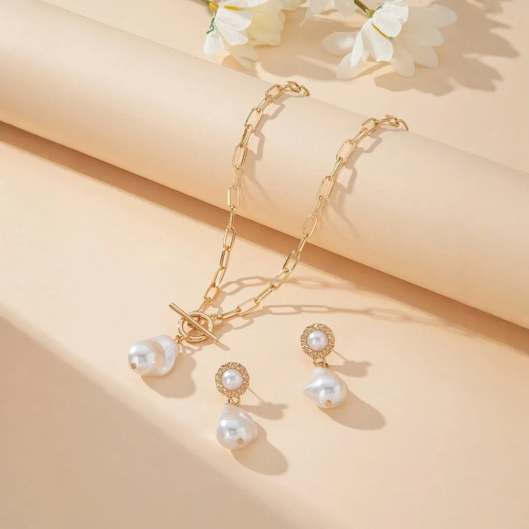 Gold-coloured baroque pearl pendant necklace and earring set on a dark background.