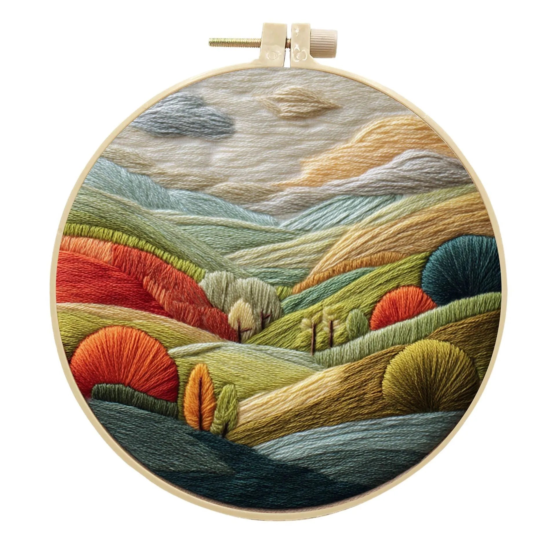 Embroidery DIY kit components: printed landscape fabric, embroidery hoop, coloured threads, and needles laid flat.