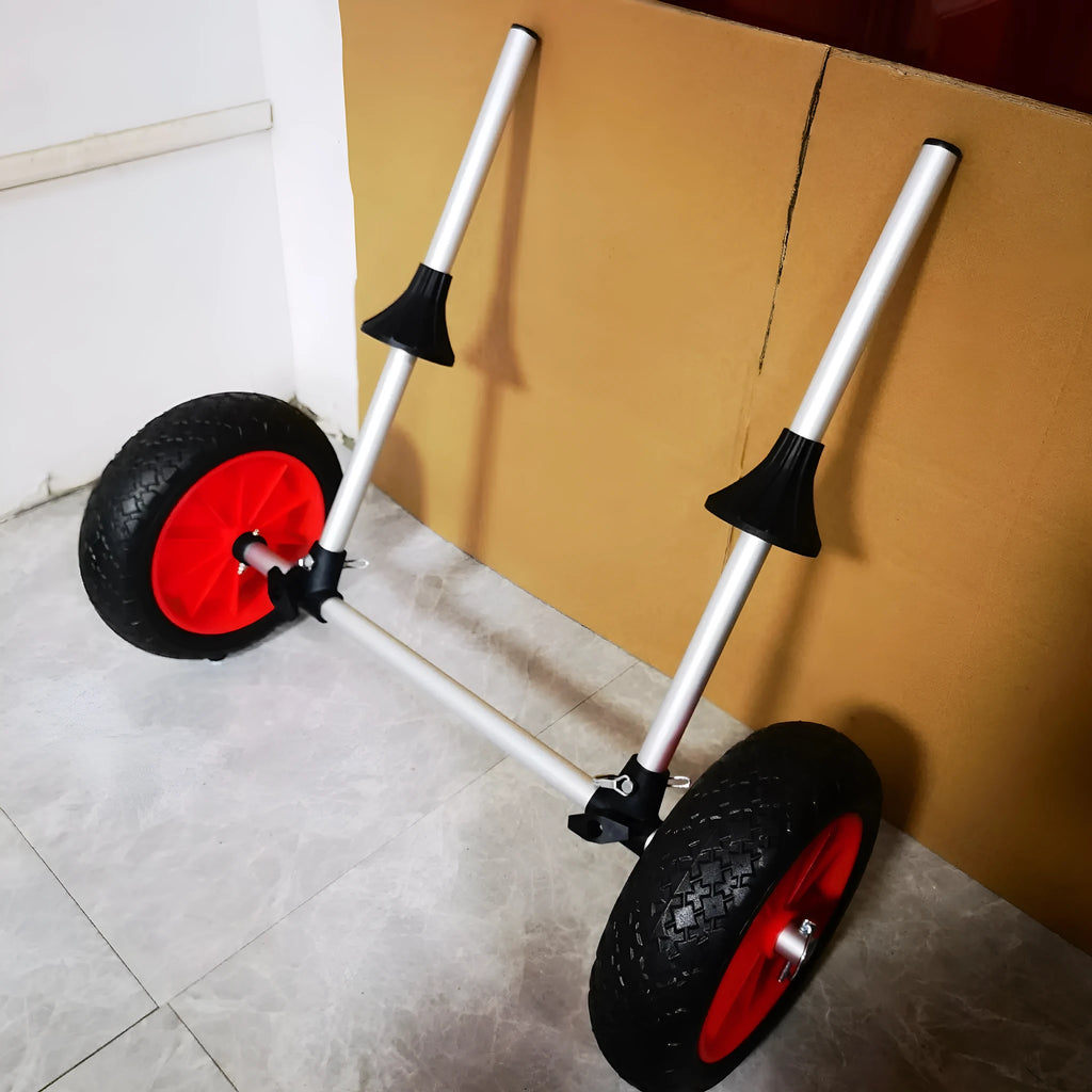 Foldable aluminium kayak cart with solid rubber tyres and black securing straps on a sandy beach.