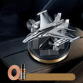 Solar-powered rotating fighter jet perfume ornament in silver, gold, blue, and red colours on a wooden surface.