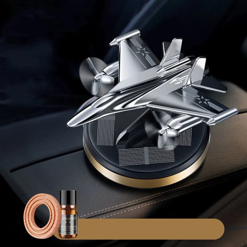 Solar-powered rotating fighter jet perfume ornament in silver, gold, blue, and red colours on a wooden surface.