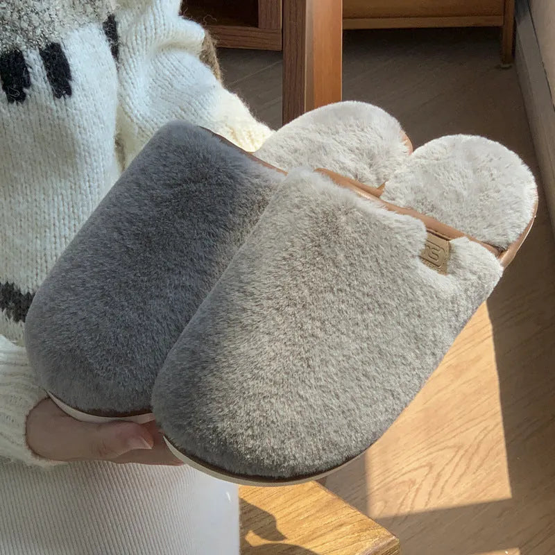 A pair of solid blue plush slip-on house slippers with a non-slip PVC sole and decorative car stitching on the upper.