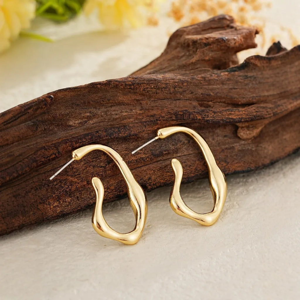 Gold irregular shaped minimalist earrings for women with a geometric silhouette on a plain background.