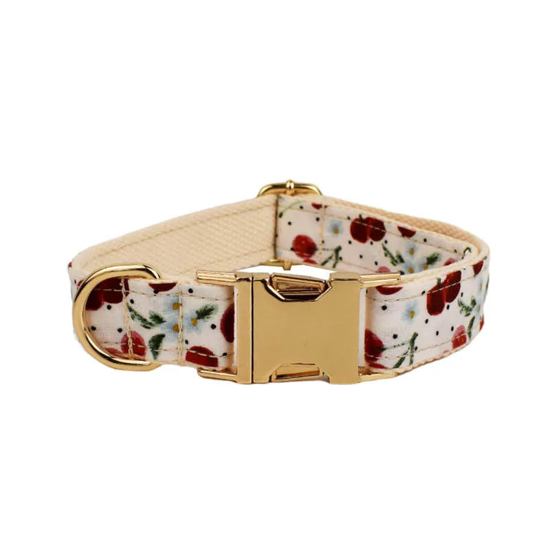 Red cherry print dog collar and leash set with light gold buckle, matching bow, vest, and poop bag.