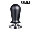 Black and red coffee tamper powder press tool with stainless steel base on a wooden table.