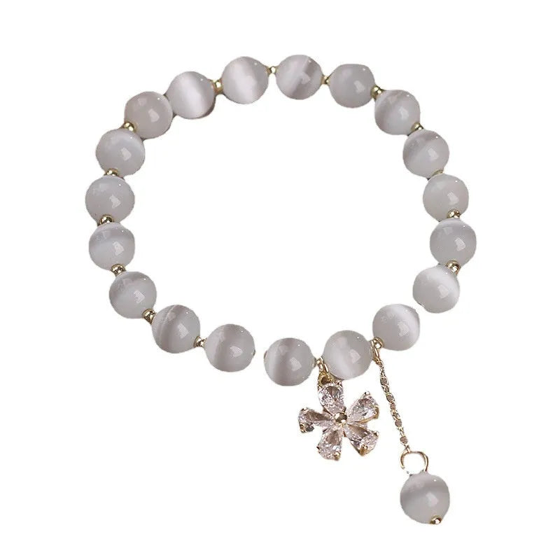 Close-up of a women's white cat's eye crystal bracelet with a flower tassel and silver safety buckle.