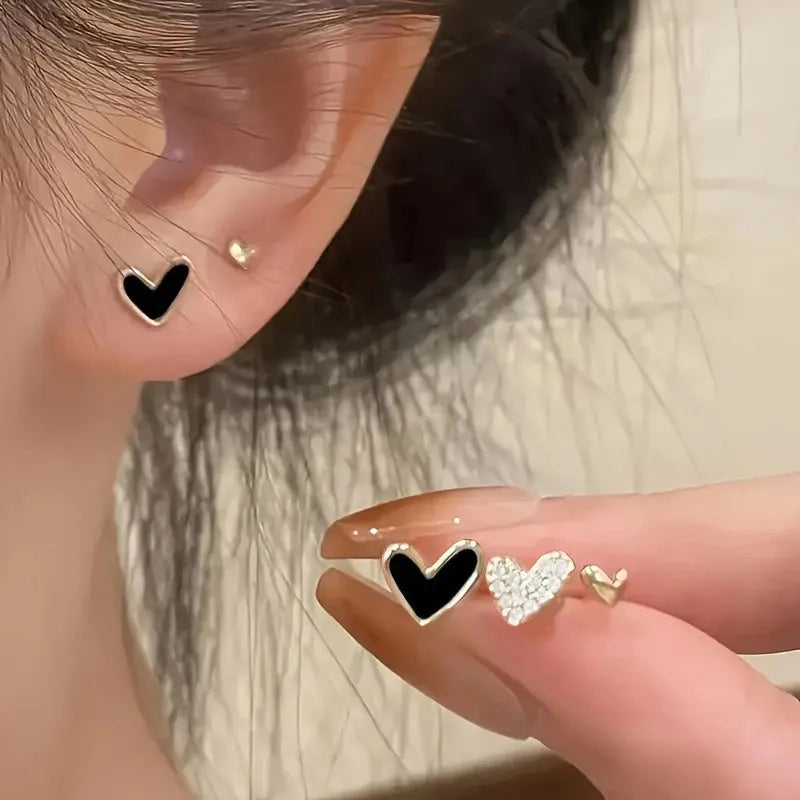 Three pairs of heart-shaped earrings in gold, black, black-white, and pink colours on display