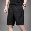 Man wearing loose-fit black printed sports shorts with an elasticated waist on a beach.
