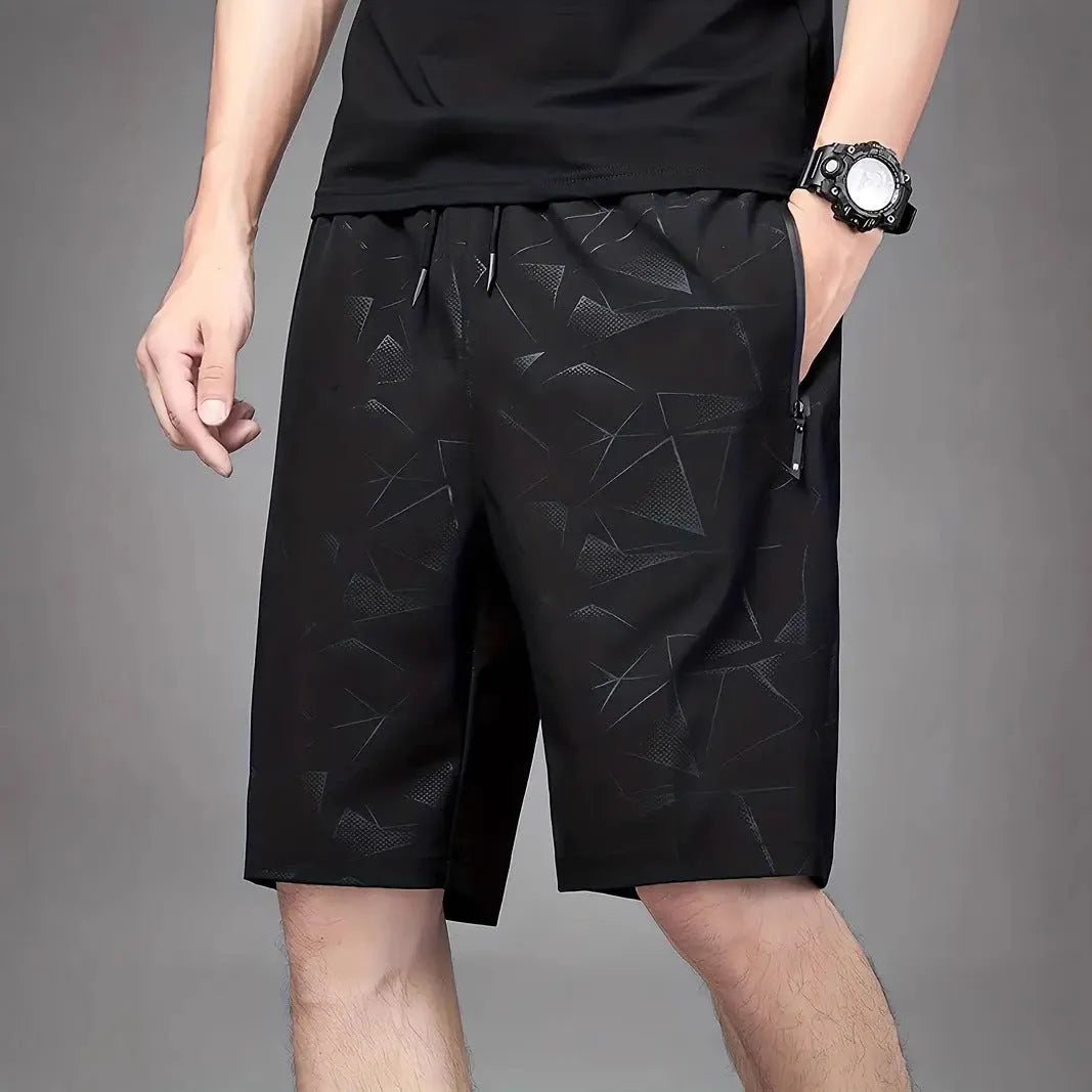 Man wearing loose-fit black printed sports shorts with an elasticated waist on a beach.