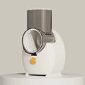 White electric vegetable slicer with rotary grater and suction base on a kitchen counter.