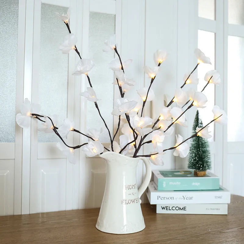 Pink fabric and plastic LED Phalaenopsis orchid branch light, 65cm long, on a table providing warm white ambient glow.