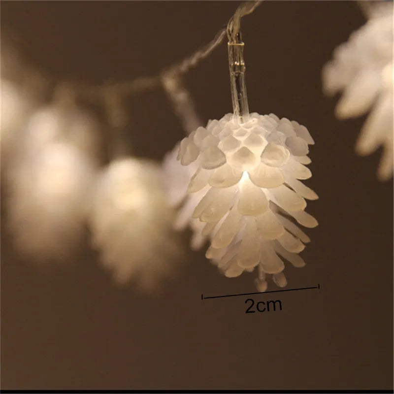 Warm white LED pine cone decorative light string powered by batteries on a green foliage background.