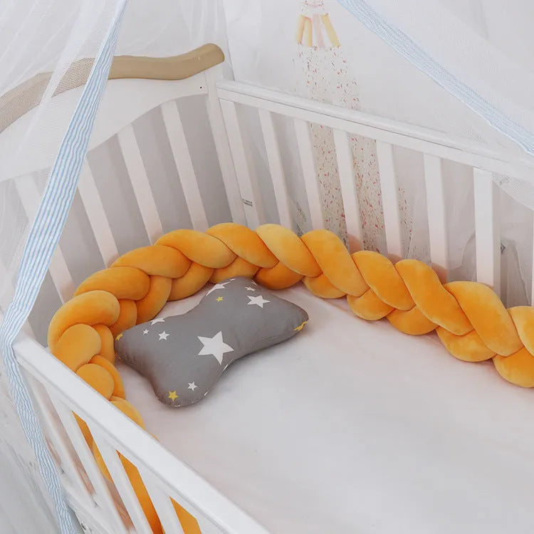 Close-up of a grey braid knot pillow cushion cot bumper fitted around white crib rails.