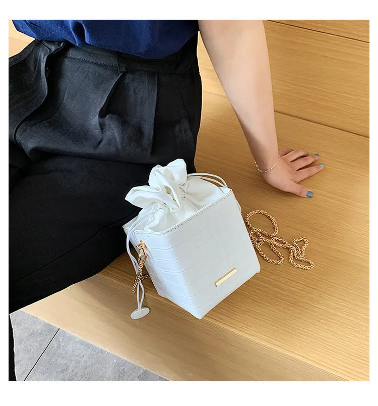 Small black bucket-shaped women's messenger bag with a drawstring top and metallic chain detail on the strap