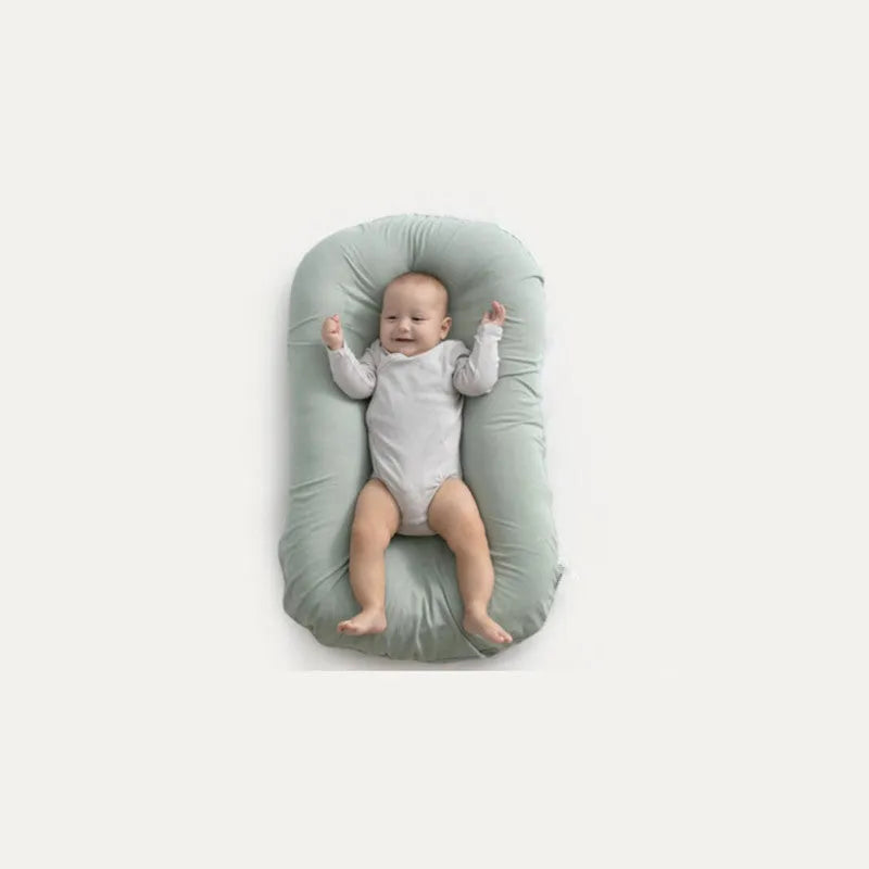 Beige portable baby nest cot crib for infants on a neutral background