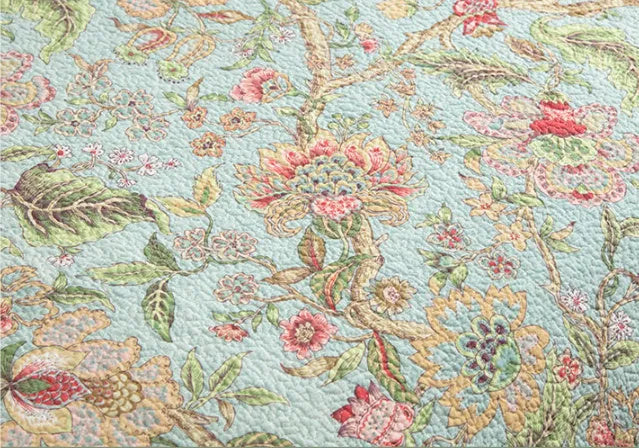 Blue American-style floral and bird quilted cotton bedspread set on a bed, showing textured stitching.