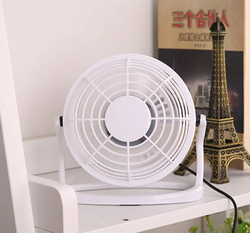 Small black and white USB desk fan with adjustable angle on a wooden table.