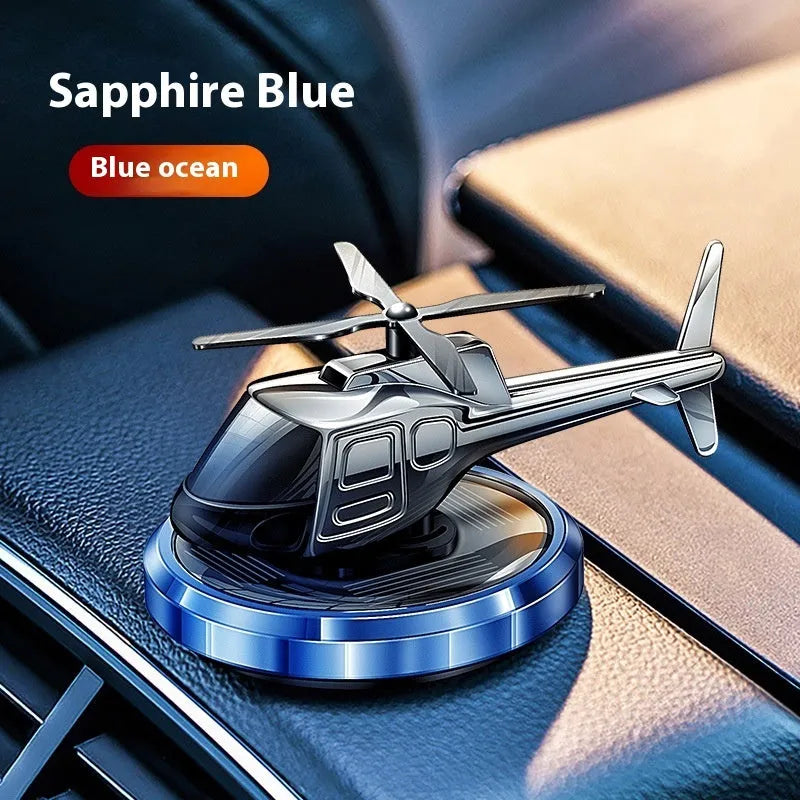 Silver metal solar-powered helicopter car air freshener rotating on a dashboard