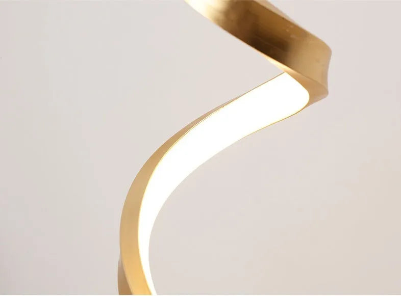 Modern LED table lamp with gold metal base and curved acrylic shade on a desk