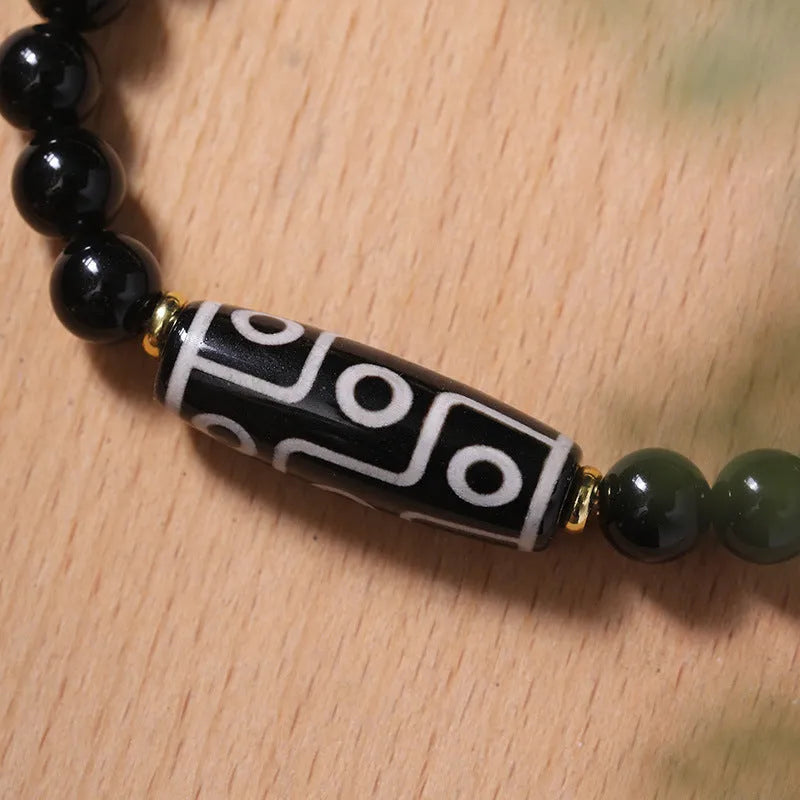 Close-up of a black obsidian dzi bead agate bracelet with adjustable cord, showing ethnic Tibetan design.