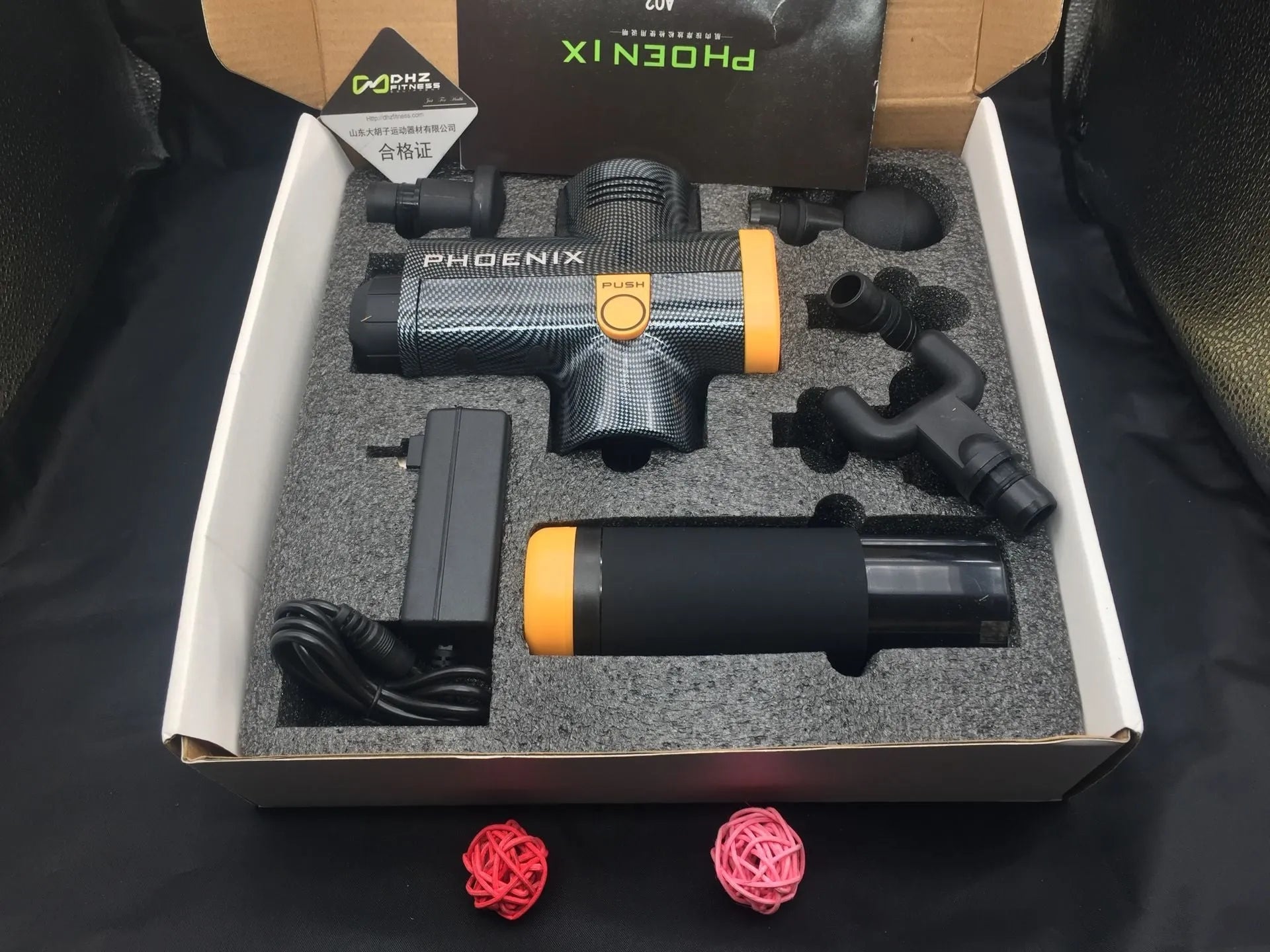 A black or silver ABS plastic percussion massage gun with four different removable massage heads on a table.