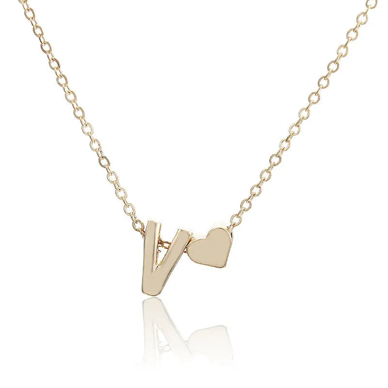 Gold tone peach heart shape pendant with a letter charm on a white background.