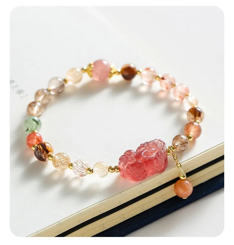 Close-up of a women's copper bracelet with a pink Strawberry Quartz crystal, a detailed Pixiu charm, and a white freshwater pearl.