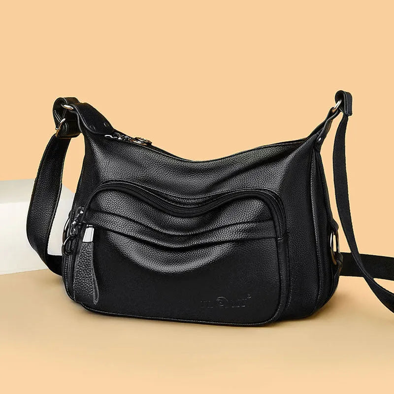 Blue horizontal square women's crossbody bag with a soft handle and zipper opening, showing organiser pockets inside.