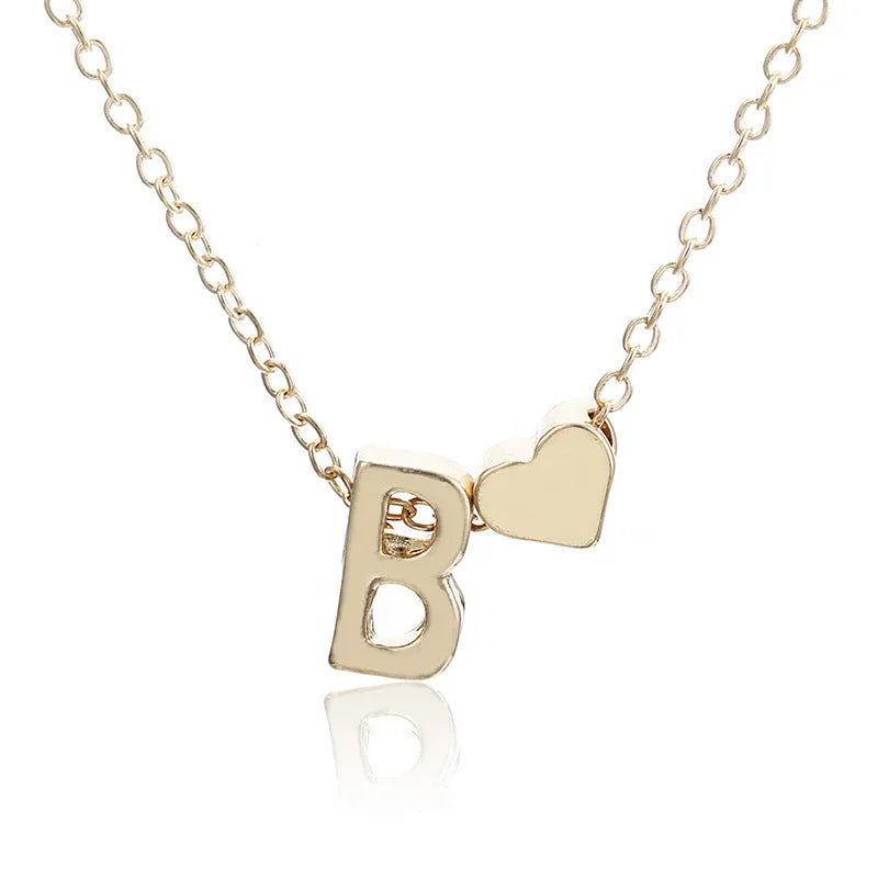 Gold tone peach heart shape pendant with a letter charm on a white background.