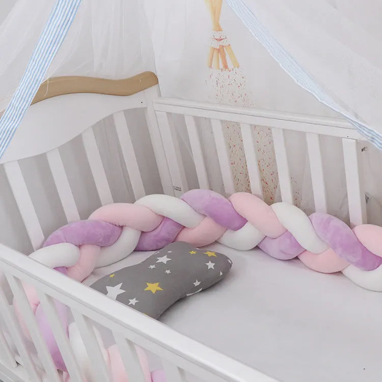 Close-up of a grey braid knot pillow cushion cot bumper fitted around white crib rails.