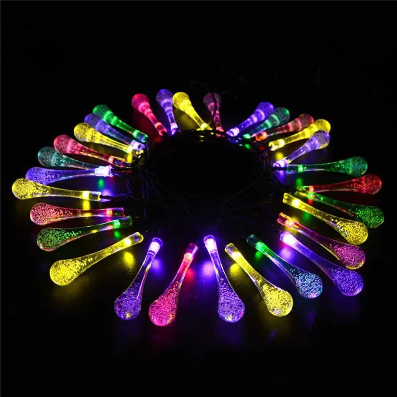 Solar-powered waterproof LED string lights with bubble drop pendants illuminating an outdoor garden space at dusk.