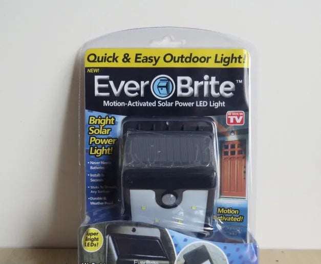 Two white solar-powered motion sensor security lights mounted on a dark wall, with adjustable lamp heads and solar panels.