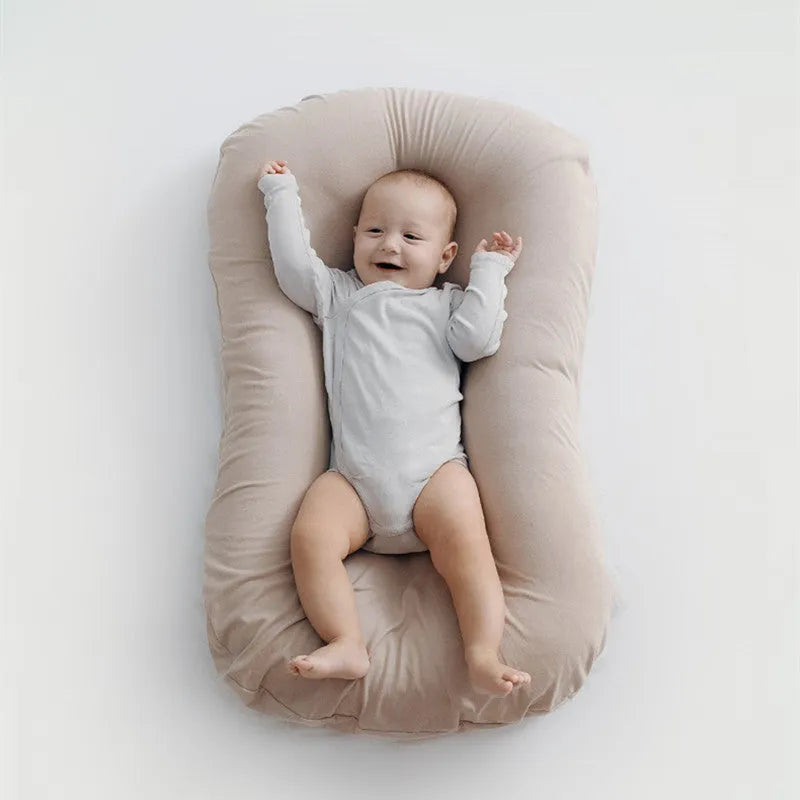 Beige portable baby nest cot crib for infants on a neutral background