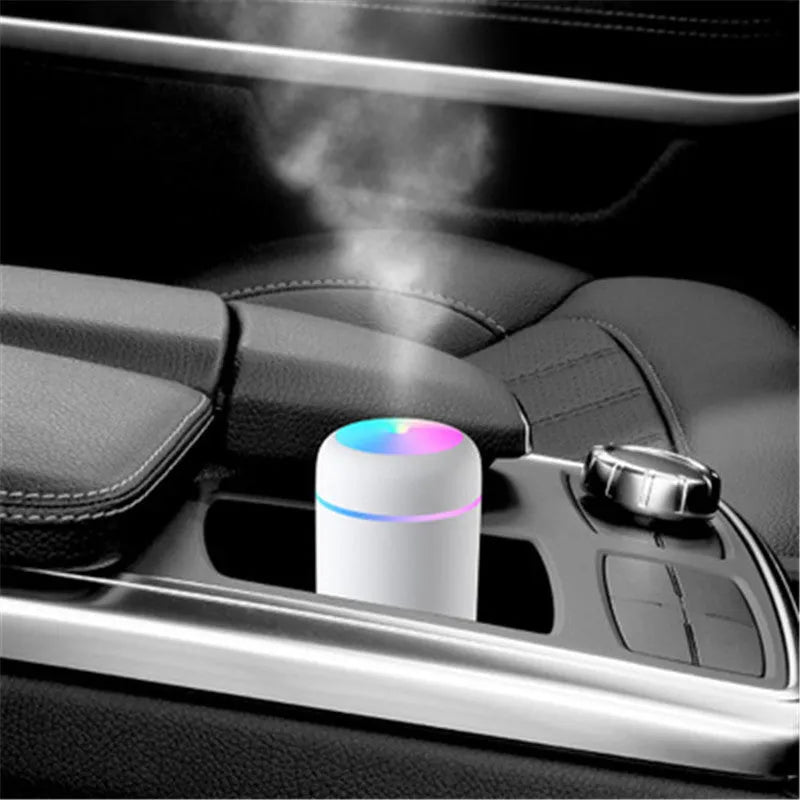 Pink portable car humidifier with coloured lights on a car dashboard next to a USB cable