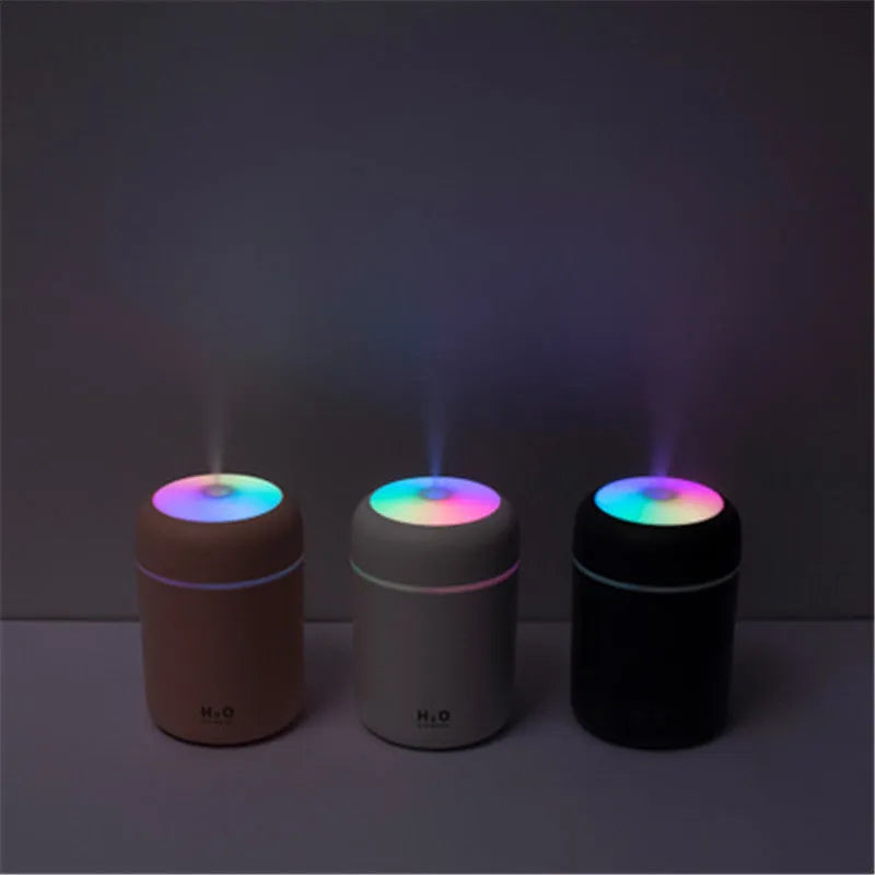 Pink portable car humidifier with coloured lights on a car dashboard next to a USB cable