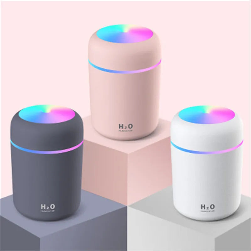 Pink portable car humidifier with coloured lights on a car dashboard next to a USB cable
