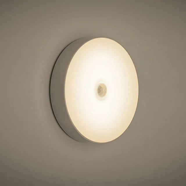Compact round beige motion sensor LED night light with USB charging cable on a wooden surface
