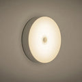 Compact round beige motion sensor LED night light with USB charging cable on a wooden surface