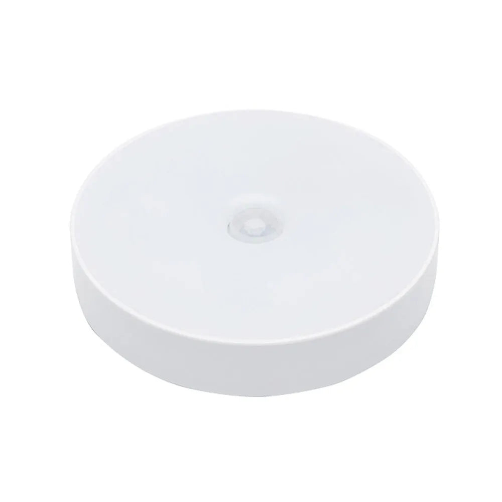 Compact round beige motion sensor LED night light with USB charging cable on a wooden surface