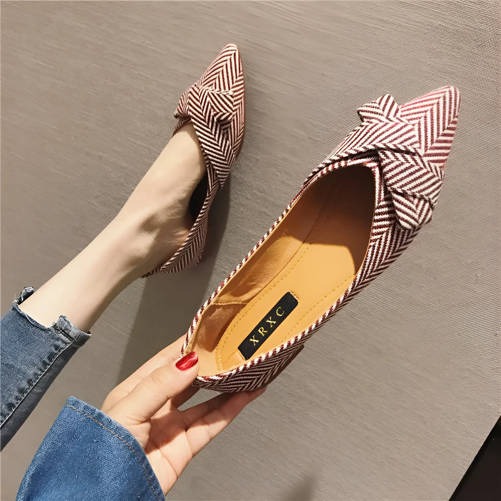 Women's black pointed toe slip-on shoes with a low flat heel on a plain background.