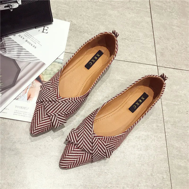 Women's black pointed toe slip-on shoes with a low flat heel on a plain background.