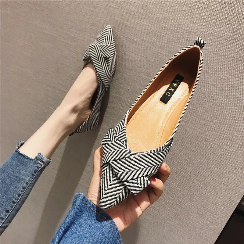 Women's black pointed toe slip-on shoes with a low flat heel on a plain background.